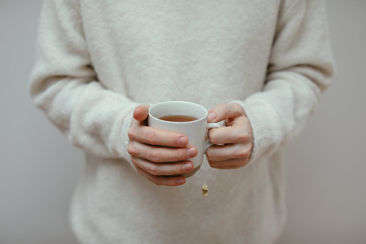 A close-up view of hands holding a hot cup of tea, dressed in a warm sweater.